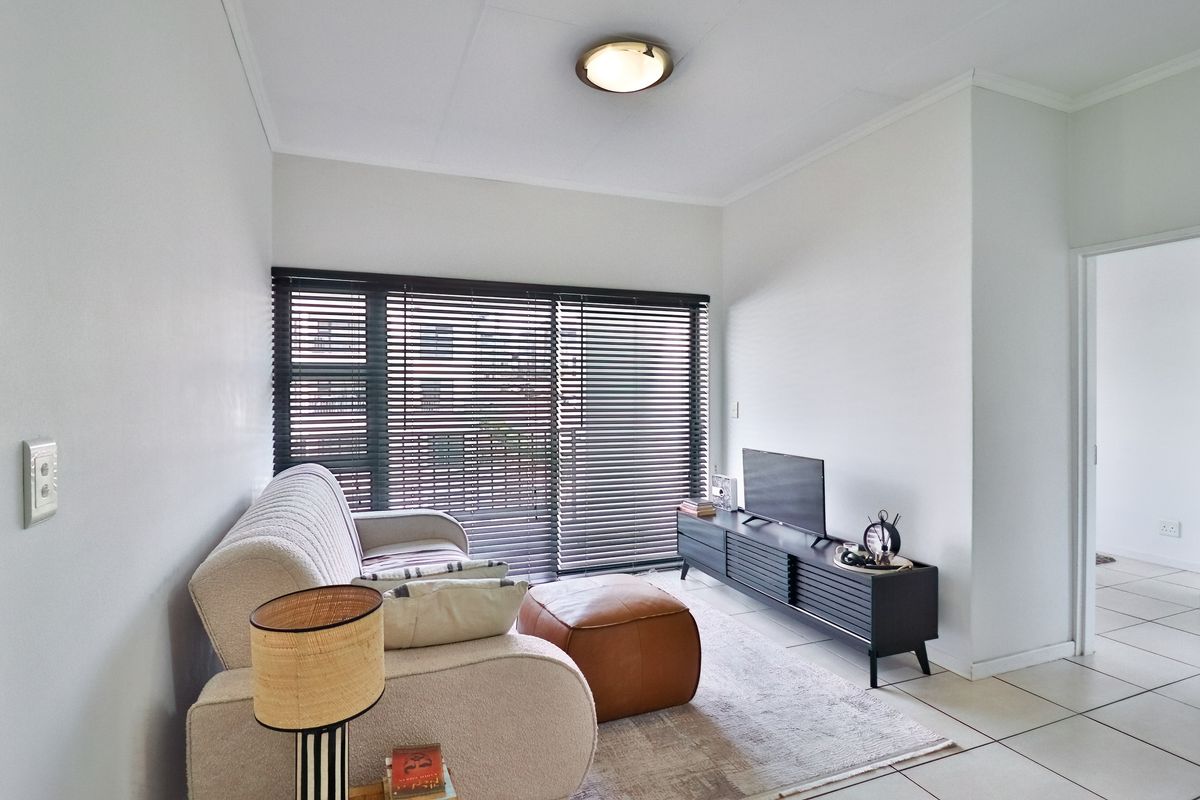 A bright living room featuring tiled flooring, a ceiling light fixture, and a large sliding glass door fitted with venetian blinds.