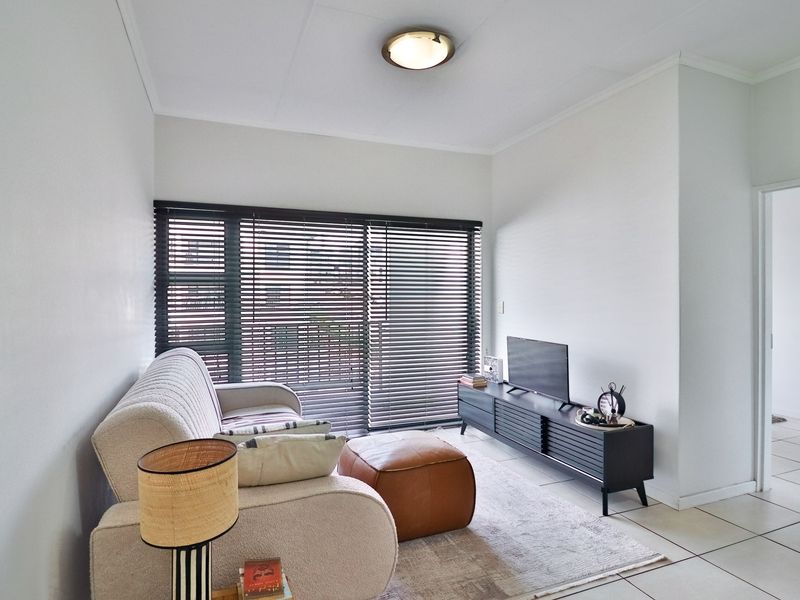 A bright living room featuring tiled flooring, a ceiling light fixture, and a large sliding glass door fitted with venetian blinds.