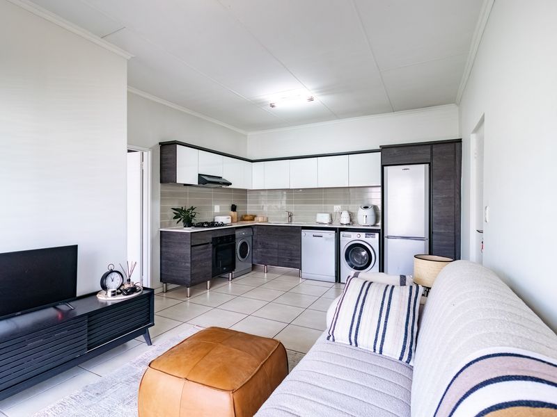 Open-plan living area featuring a modern kitchen with built-in cabinetry, tiled flooring, and integrated appliances, seamlessly connected to the lounge space.