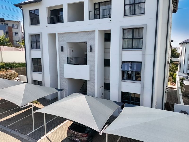 A modern multi-story townhouse complex featuring a paved parking area with shade cloth carports and well-maintained exterior facade with balconies.