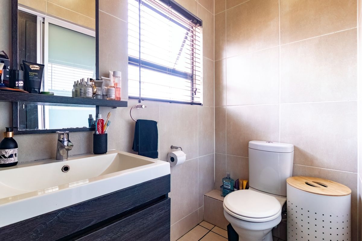 A modern, well-maintained bathroom featuring a sleek vanity with basin, wall-mounted mirror, toilet, and neutral floor-to-ceiling wall tiles.
