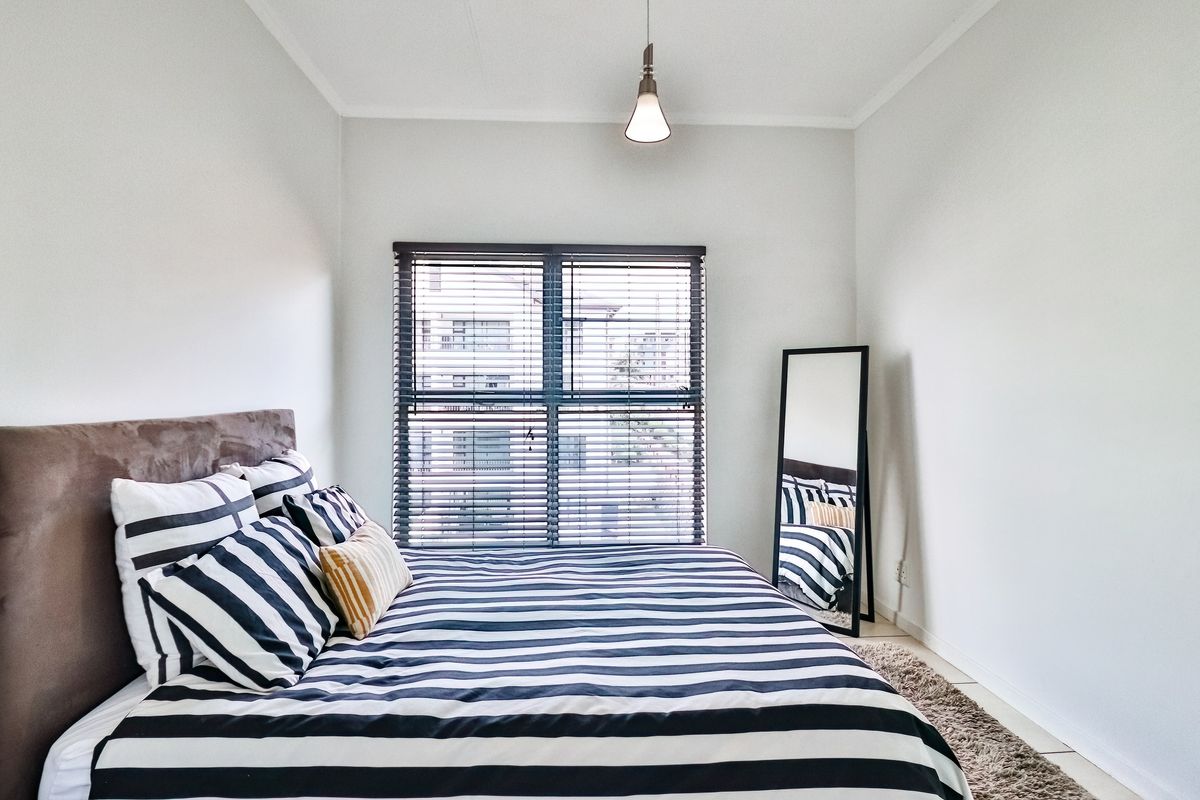 A well-maintained bedroom featuring neutral walls, tiled flooring, a central pendant light, and venetian blinds on the window.