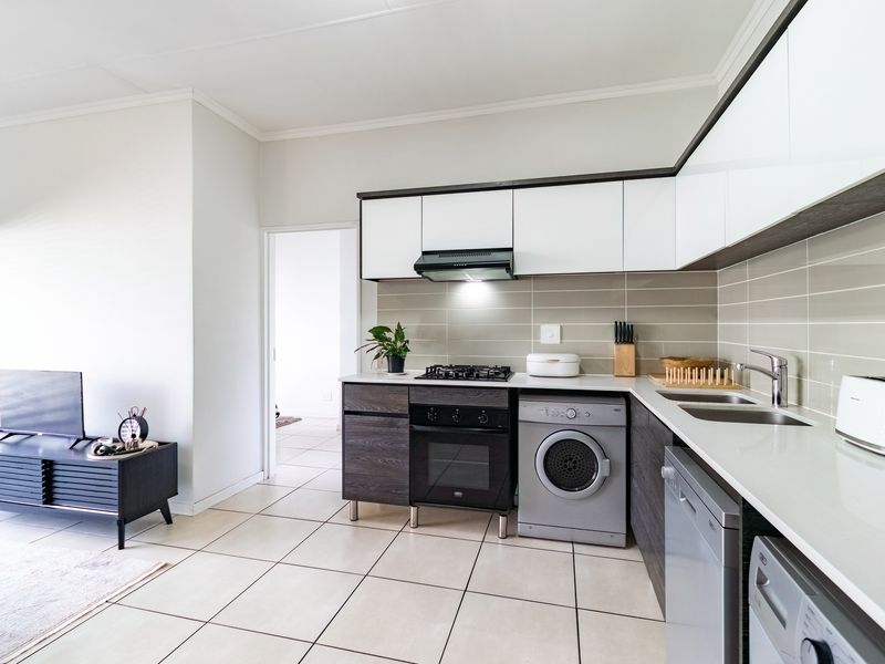 Modern open-plan kitchen featuring sleek two-tone cabinetry, gas hob, integrated oven, and tiled flooring, seamlessly flowing into the adjacent living area.