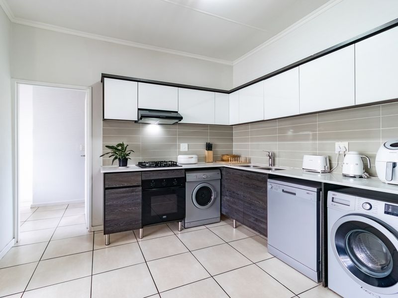 Modern kitchen featuring two-tone cabinetry, gas hob, electric oven, extractor fan, tiled backsplash, and integrated space for laundry appliances.