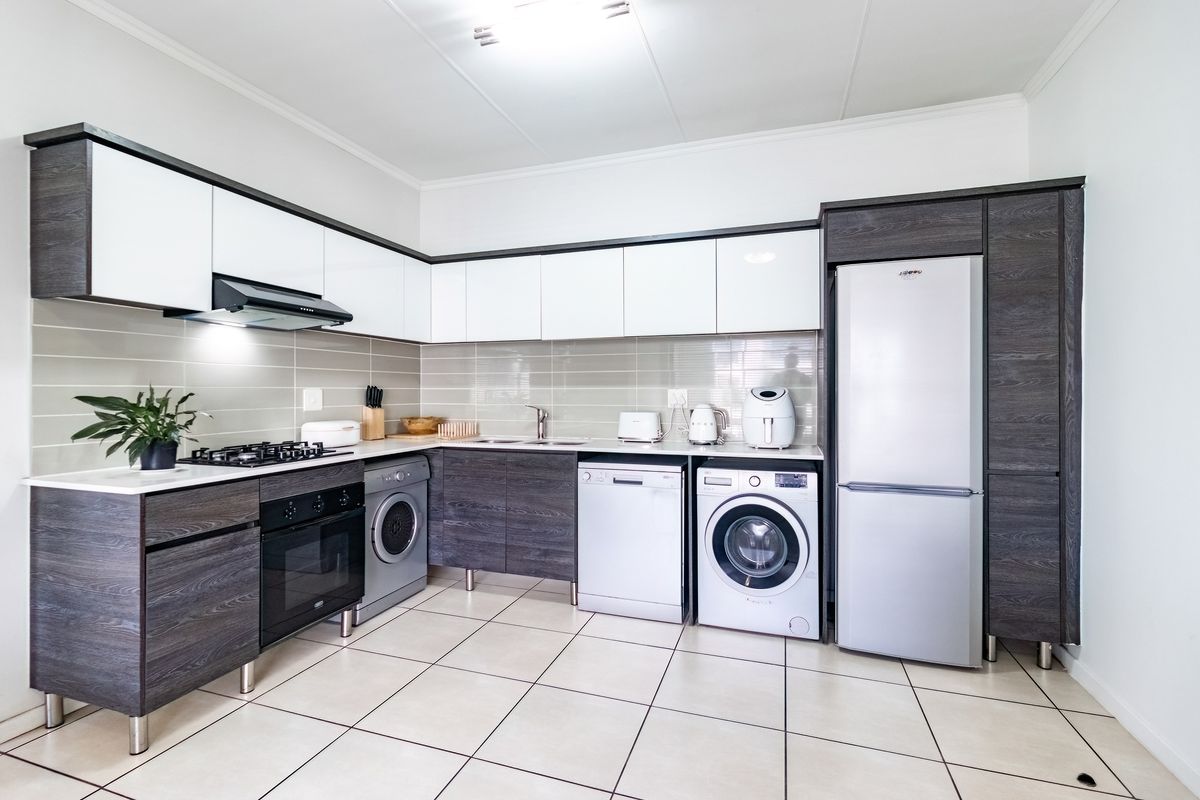 Modern kitchen featuring two-tone cabinetry, gas hob, extractor fan, built-in oven, and tiled flooring with integrated space for laundry appliances.