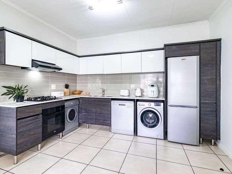 Modern kitchen featuring two-tone cabinetry, gas hob, extractor fan, built-in oven, and tiled flooring with integrated space for laundry appliances.