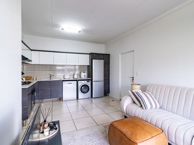 An open-plan living area featuring a modern kitchen with built-in cabinetry, tiled flooring, and integrated appliances, seamlessly flowing into the lounge space.