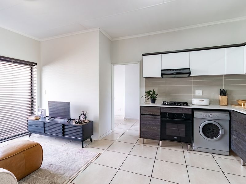 Modern open-plan living area featuring a compact kitchen with built-in cabinetry, gas hob, oven, and tiled flooring throughout.