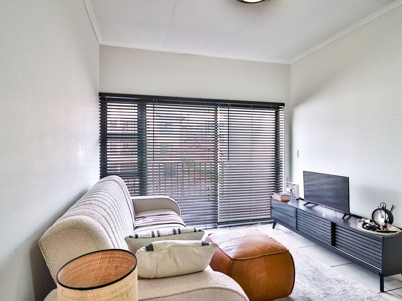 A bright living room featuring tiled flooring, neutral walls, and large sliding glass doors fitted with dark venetian blinds.