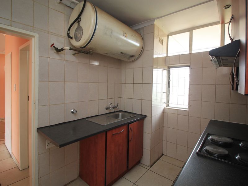 A compact kitchen featuring built-in cabinetry, a stainless steel sink, an electric hob, and an exposed wall-mounted water heater.