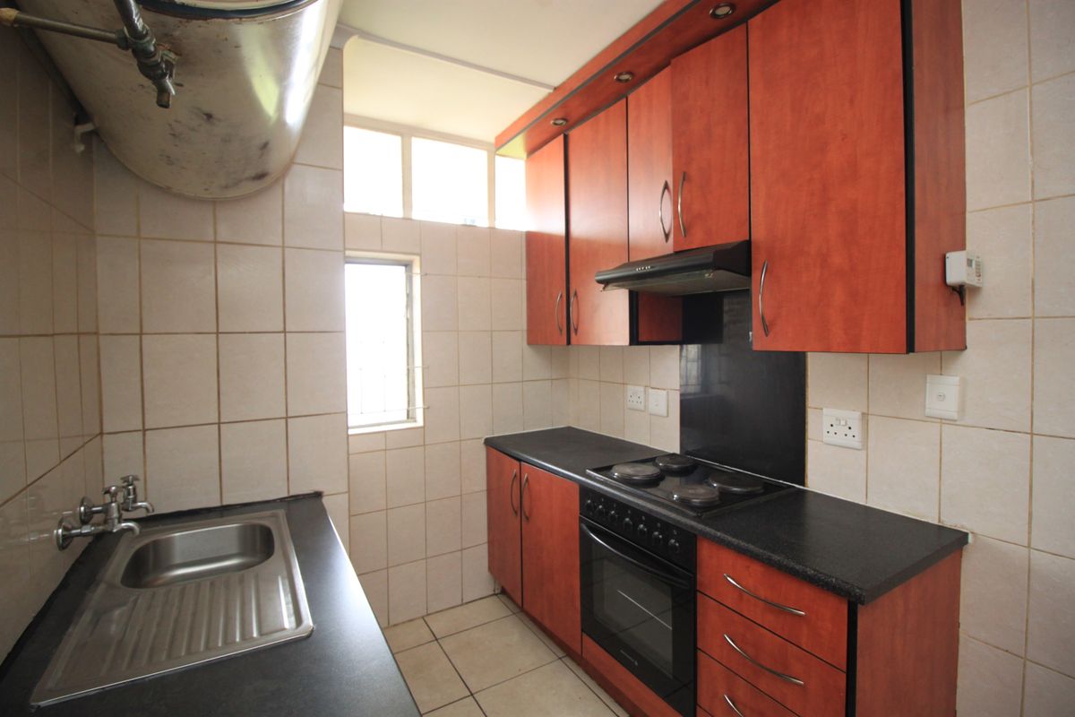 A functional kitchen featuring wood-finish cabinetry, dark countertops, built-in oven and hob, and tiled surfaces throughout.