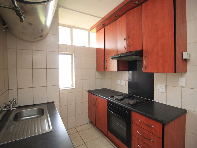 A functional kitchen featuring wood-finish cabinetry, dark countertops, built-in oven and hob, and tiled surfaces throughout.