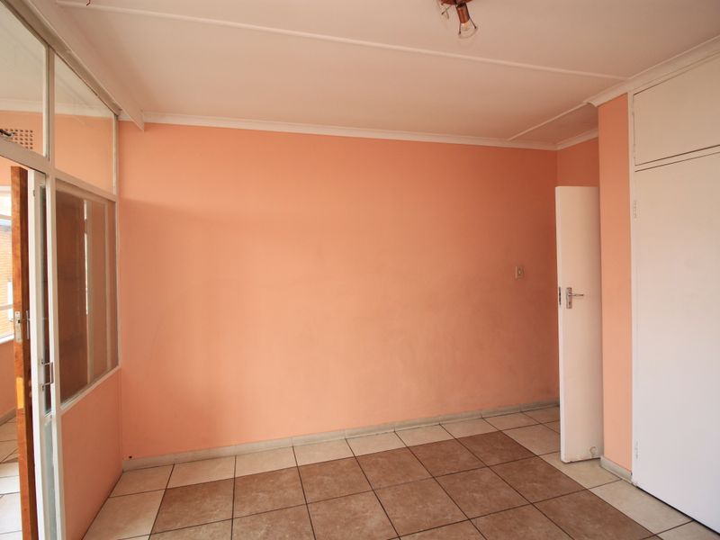 An empty bedroom featuring tiled flooring, a built-in cupboard, and a glass partition wall, offering a blank canvas for renovation.