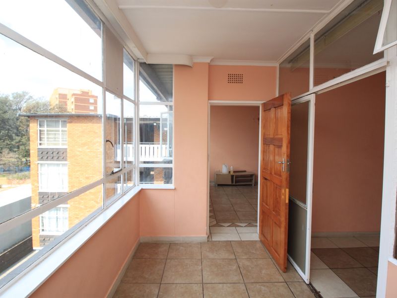 An enclosed balcony area featuring tiled flooring and large windows, providing a bright transition space between the interior rooms.