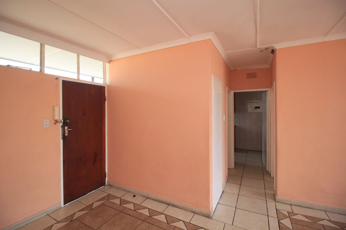 An empty entrance foyer featuring tiled flooring, a solid wood front door with transom window, and access to the interior hallway.