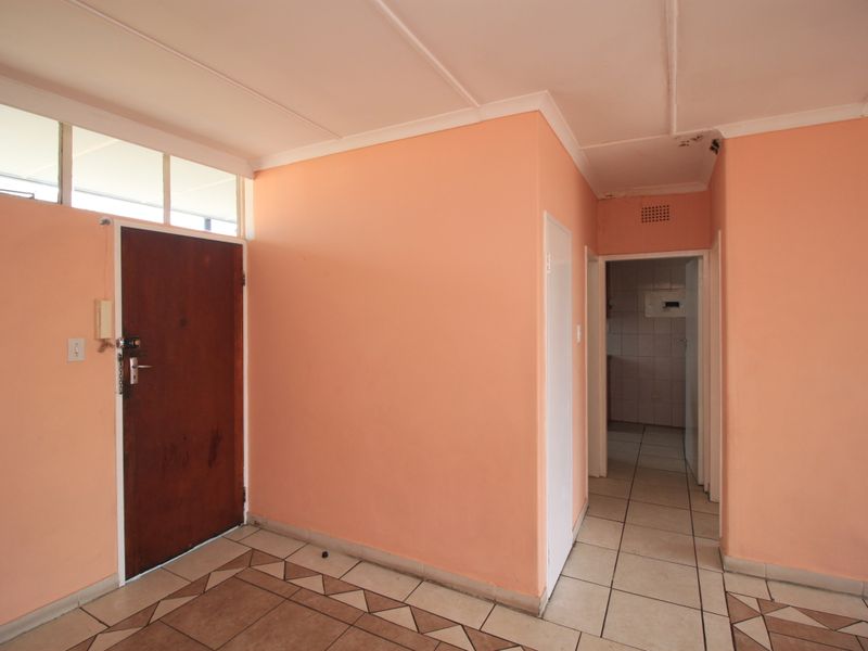 An empty entrance foyer featuring tiled flooring, a solid wood front door with transom window, and access to the interior hallway.