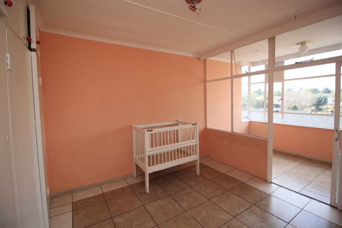 A bedroom featuring tiled flooring, a glass partition wall, and a built-in cupboard, offering a bright space with potential for modernization.