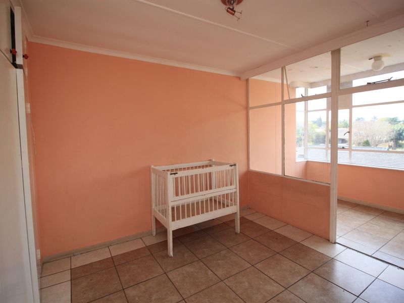 A bedroom featuring tiled flooring, a glass partition wall, and a built-in cupboard, offering a bright space with potential for modernization.
