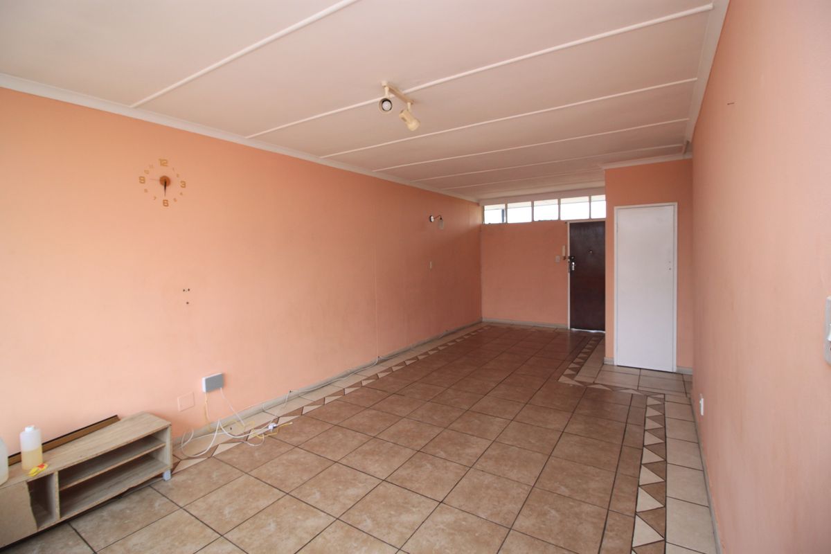 An empty living room featuring tiled flooring with decorative borders, peach-toned walls, and ceiling paneling, offering a blank canvas for renovation.