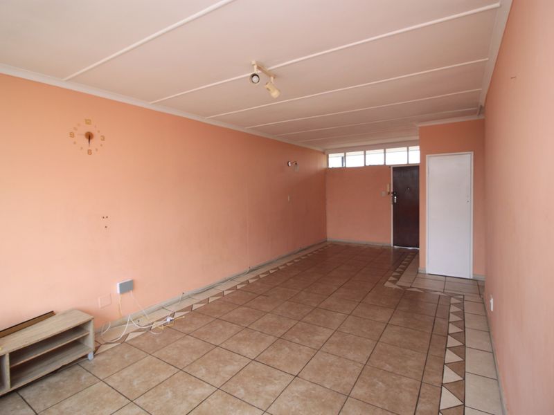 An empty living room featuring tiled flooring with decorative borders, peach-toned walls, and ceiling paneling, offering a blank canvas for renovation.