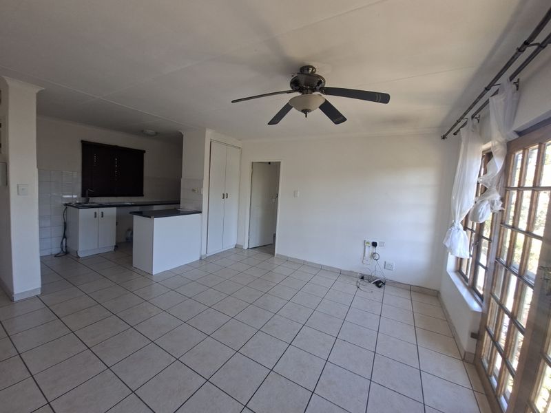 An open-plan living and kitchen area featuring tiled flooring, a ceiling fan, built-in cabinetry, and glass doors leading to the exterior.