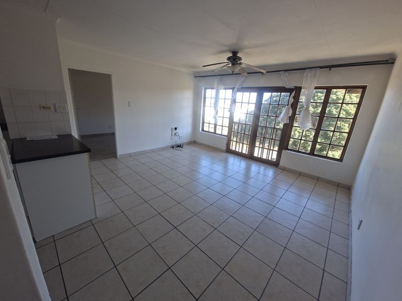 Spacious open-plan living area featuring tiled flooring, a ceiling fan, and large timber-framed glass doors leading to an outdoor space.