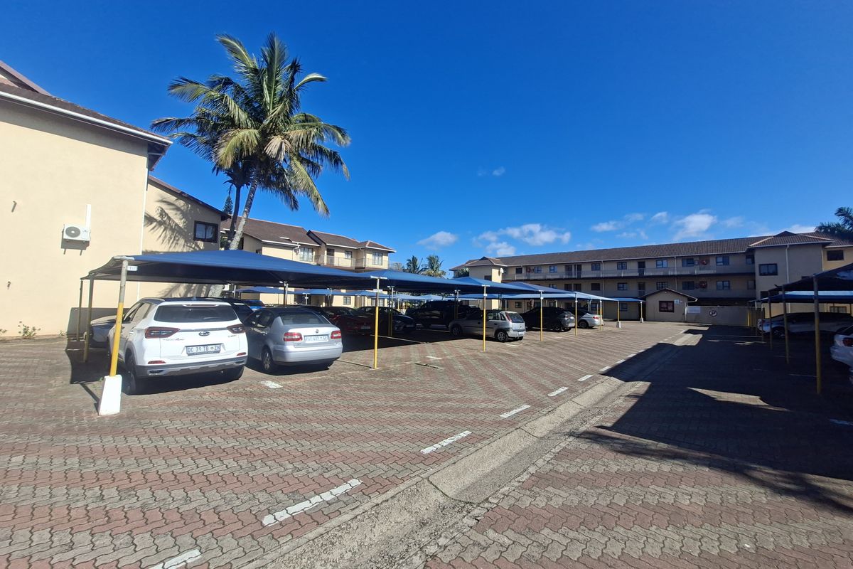 Exterior view of the apartment complex parking area featuring paved surfaces and covered shade cloth parking bays.