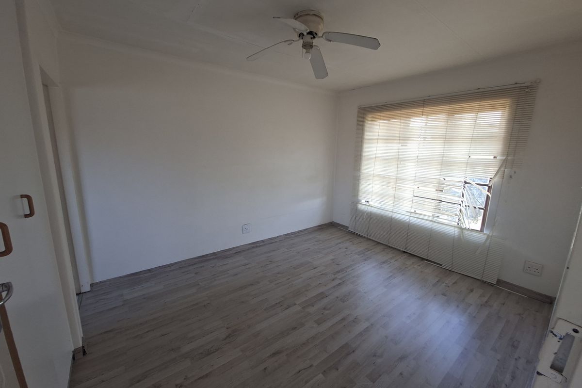 An empty bedroom featuring laminate flooring, a ceiling fan, and venetian blinds covering the window.