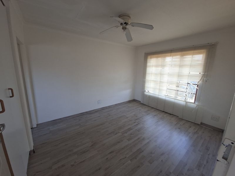 An empty bedroom featuring laminate flooring, a ceiling fan, and venetian blinds covering the window.
