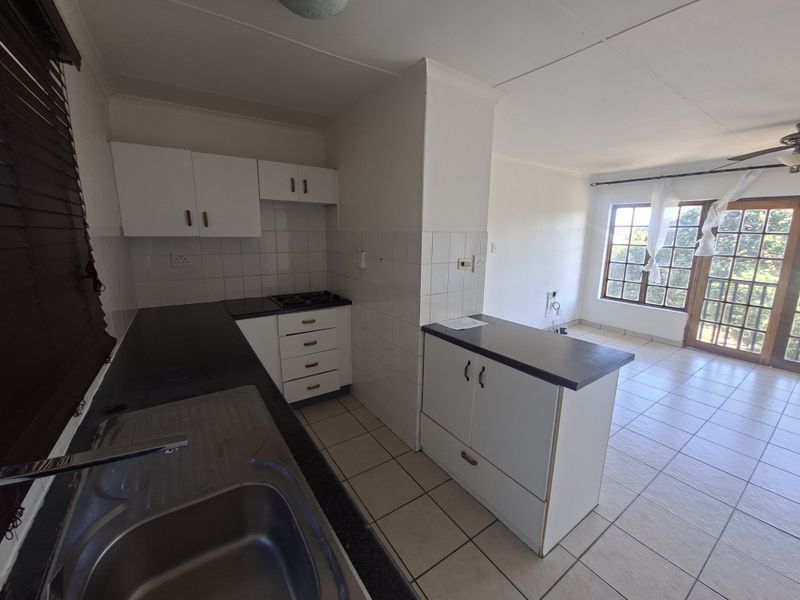 Open-plan kitchen and living area featuring tiled flooring, built-in cabinetry with laminate countertops, a gas hob, and access to a balcony through sliding doors.