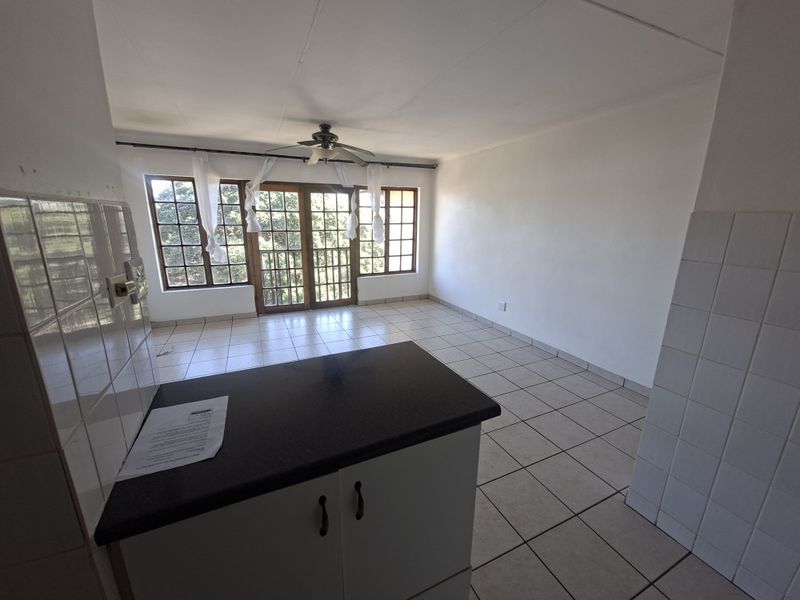Open-plan living and kitchen area featuring tiled flooring, a ceiling fan, and large windows with access to a balcony through french doors.