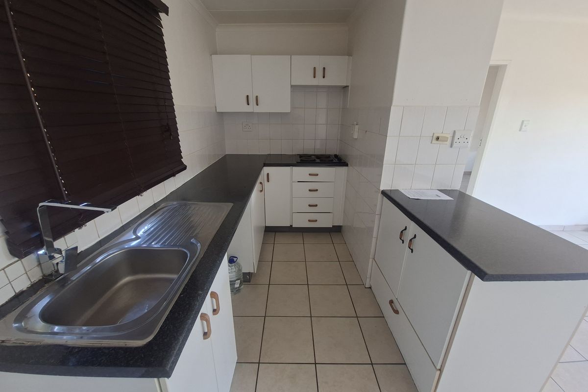 A functional kitchen featuring white cabinetry, dark laminate countertops, a stainless steel sink, and ceramic tile flooring.
