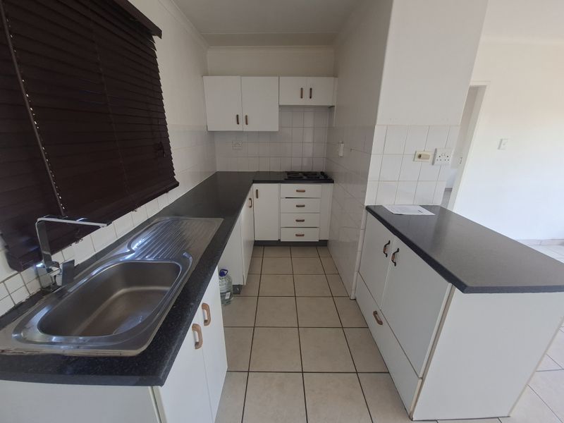 A functional kitchen featuring white cabinetry, dark laminate countertops, a stainless steel sink, and ceramic tile flooring.