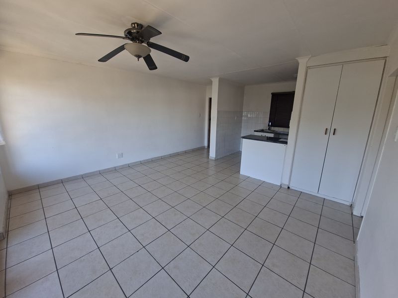 An open-plan living area featuring tiled flooring, a ceiling fan, and built-in storage cupboards, with an adjacent kitchen counter area.