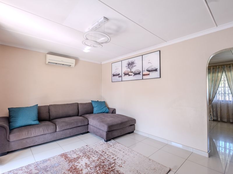 A well-maintained living room featuring tiled flooring, a split-system air conditioner, and an arched entryway leading to an adjacent space.