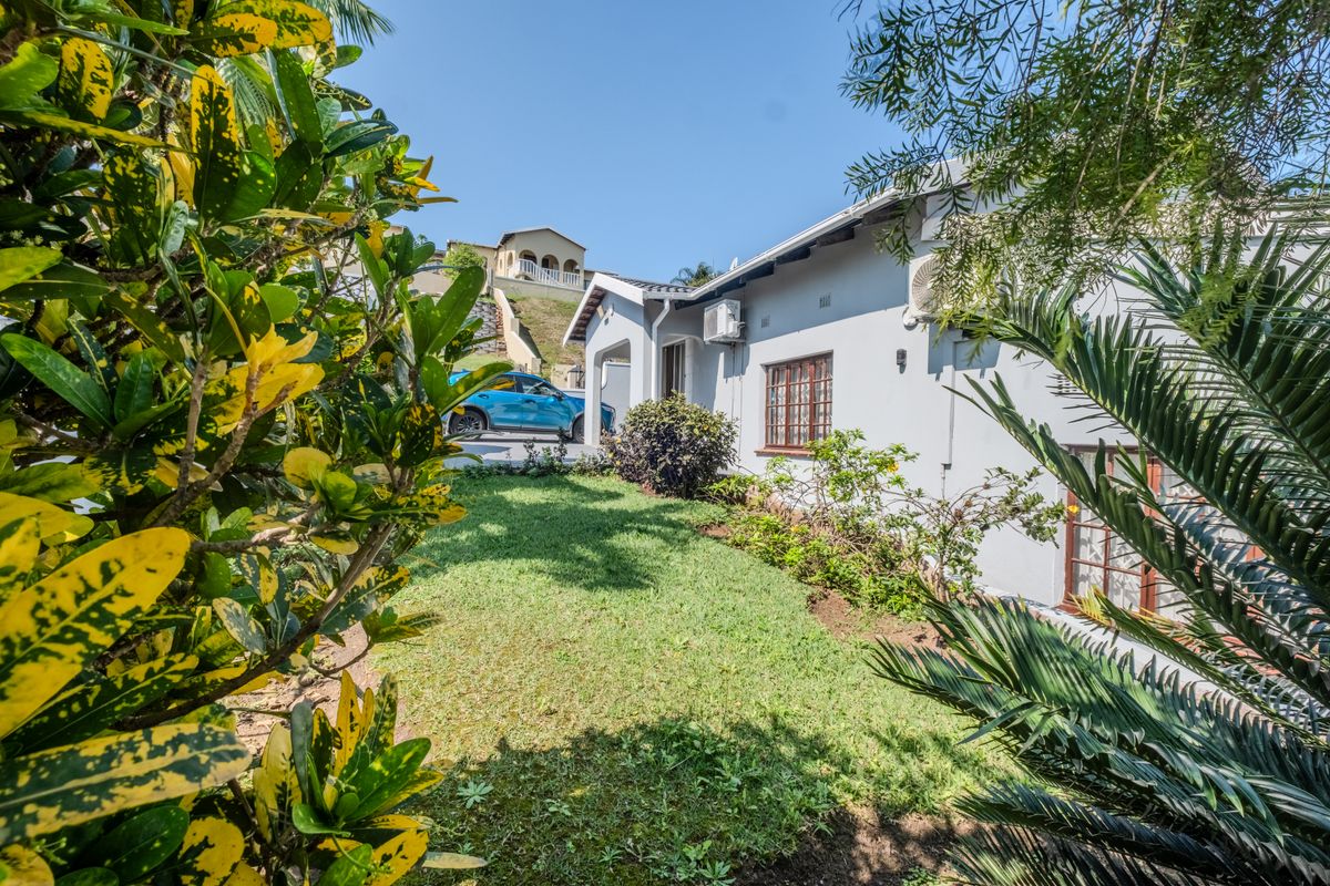 A view of the rear exterior of the house featuring a well-maintained lawn, landscaped garden, and exterior wall-mounted air conditioning unit.