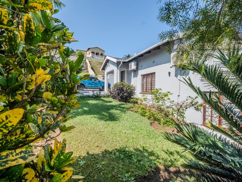 A view of the rear exterior of the house featuring a well-maintained lawn, landscaped garden, and exterior wall-mounted air conditioning unit.
