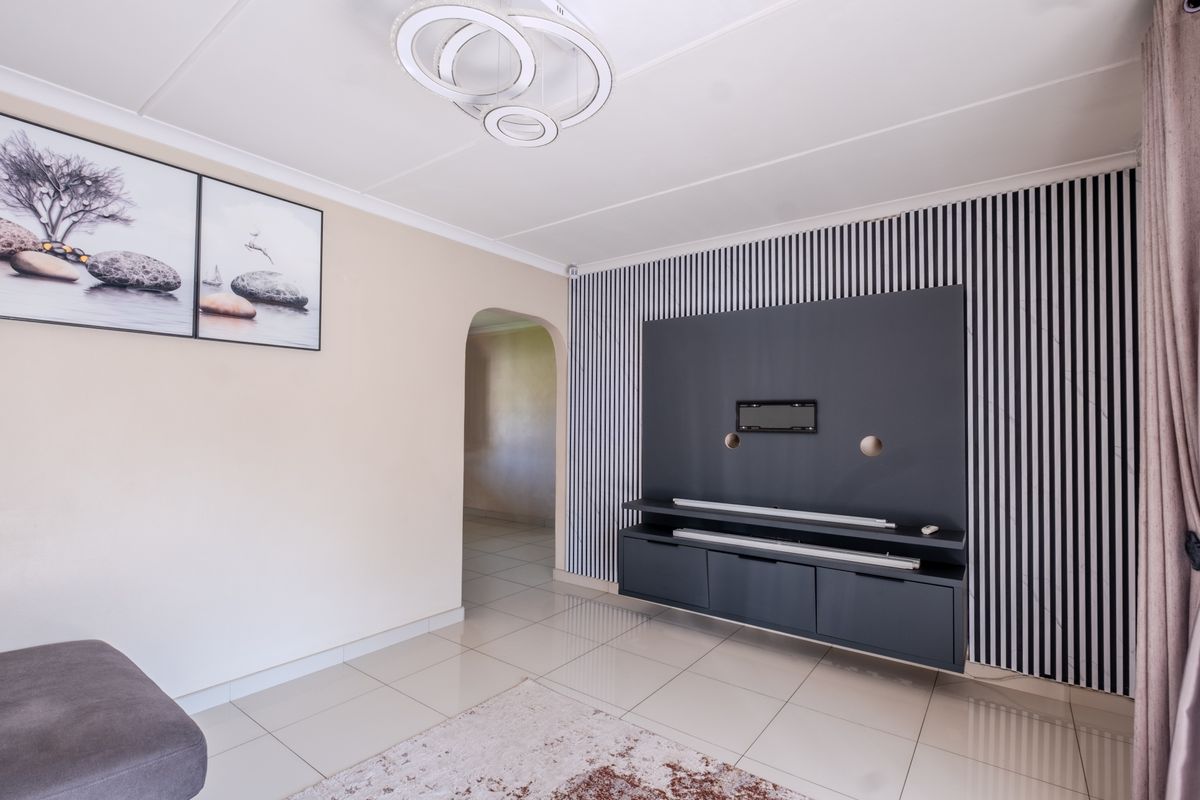 A modern living room featuring tiled floors, a built-in media console with decorative wall paneling, and an arched entryway leading to adjacent spaces.