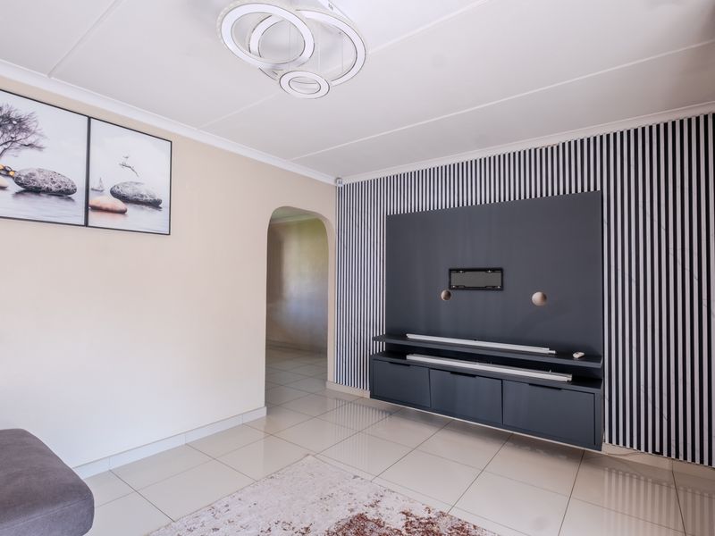 A modern living room featuring tiled floors, a built-in media console with decorative wall paneling, and an arched entryway leading to adjacent spaces.