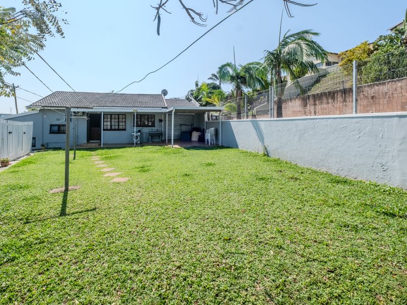 Rear view of the property featuring a covered patio, a spacious lawn, and secure perimeter walling with fencing.