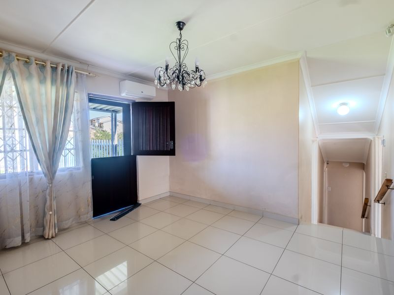 An open-plan living area featuring tiled flooring, a split-system air conditioner, and direct access to an external security door and staircase.