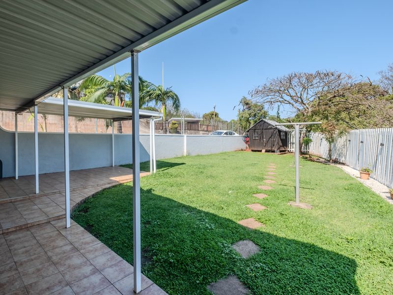 A covered patio area with tiled flooring overlooking a spacious backyard featuring a lawn, perimeter fencing, and a garden shed.