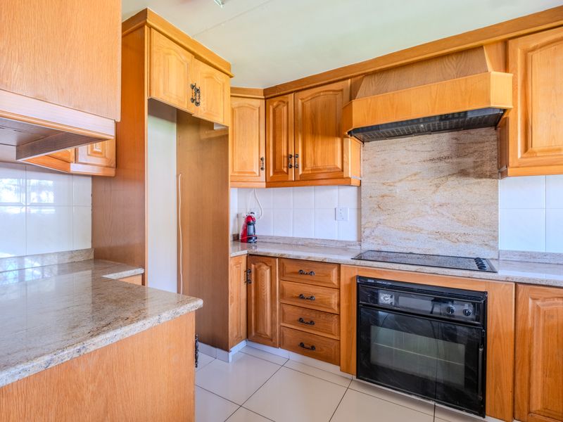 A functional kitchen featuring traditional wooden cabinetry, granite countertops, a built-in oven, and an electric hob with an integrated extractor fan.