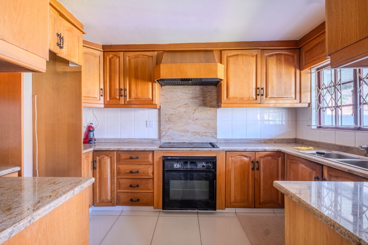 A functional kitchen featuring warm-toned wooden cabinetry, granite countertops, a built-in oven with hob, and a double basin sink.