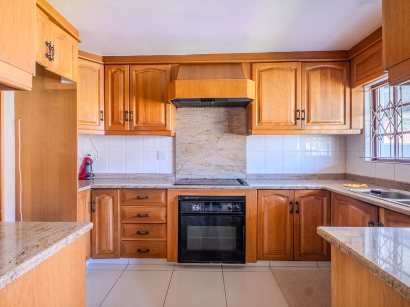 A functional kitchen featuring warm-toned wooden cabinetry, granite countertops, a built-in oven with hob, and a double basin sink.