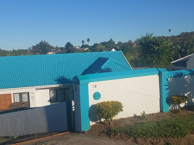 Front exterior view of the property featuring a bright blue metal roof and a secure boundary wall with a gated entrance.