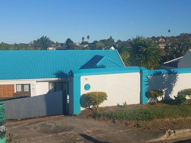 Front exterior view of the property featuring a bright blue metal roof, white boundary wall, and paved driveway access.