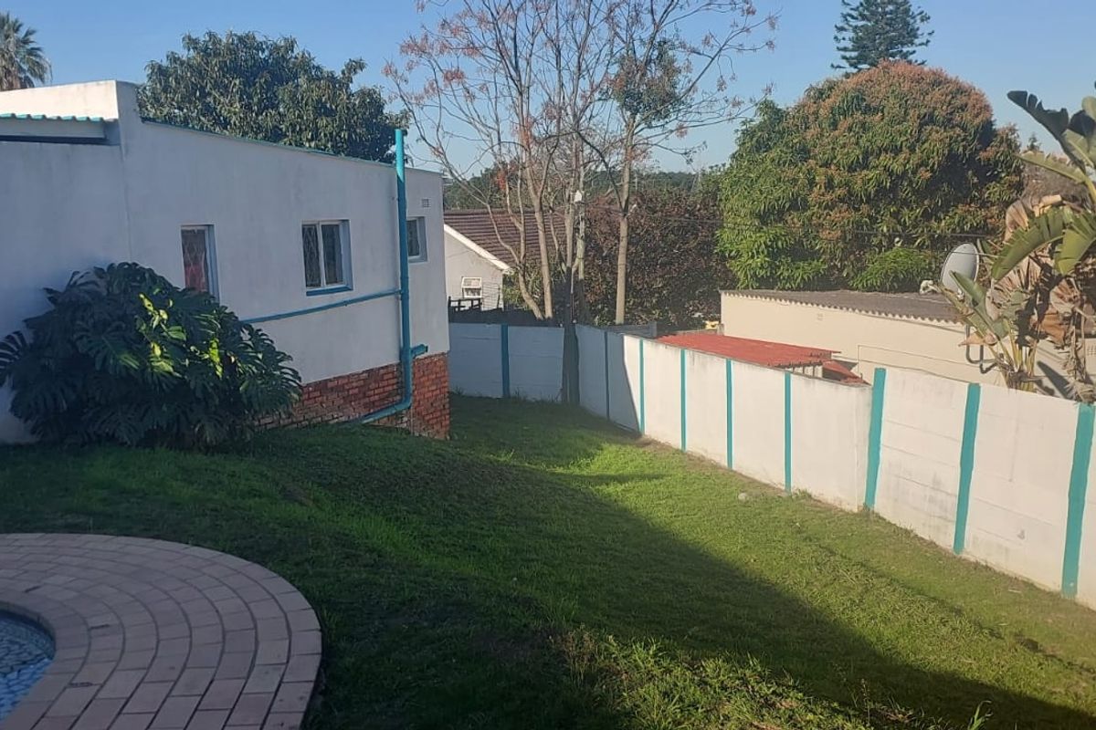 Rear garden area featuring a swimming pool with brick coping, a sloped lawn, and perimeter boundary walling.