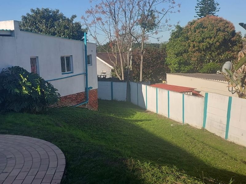 Rear garden area featuring a swimming pool with brick coping, a sloped lawn, and perimeter boundary walling.