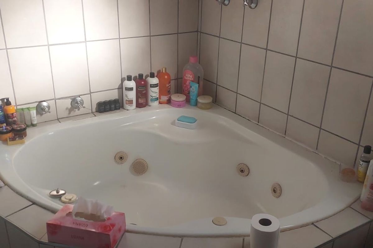 A corner spa bath featuring tiled wall surrounds and integrated jets, requiring minor maintenance to grout and fixtures.